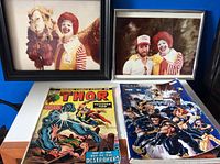 Framed photos of Ronald McDonald with a camel and another man, alongside two comic books: Thor and Ultimate Men.