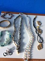 Top-down image of assorted jewelry including multiple necklaces, bracelets, and earrings arranged on white surface