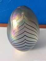 Front view of the glass paperweight showing the iridescent colors and pulled feather pattern.