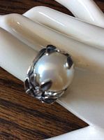Front angled view of sterling silver ring featuring a large, smooth white pearl held by intricate claw-like prongs, displayed on a white hand model over a wooden surface.