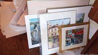 Multiple pieces of original and signed artwork leaning against a wall, showing a variety of framed and matted art pieces.