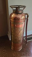Full view of vintage Red Star copper and brass fire extinguisher showing overall shape and hose attachment.