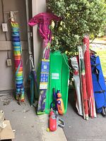 Photo showing several camping and outdoor items against a wall including colorful umbrellas, a green sled, water blasters, and a kite.