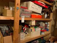 Shelves holding labeled boxes containing glass balls, Christmas tree decorations, and other boxed items, along with Santa figurines and small decorative houses on the shelf.