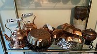 Photo showing copper kettles, jelly molds with embossed birds, and pottery vase on a shelf.