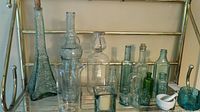Full view of various vintage glass bottles and jars with different shapes, sizes, and a white mortar and pestle.