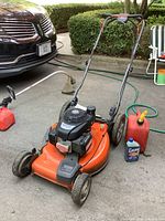Full view of mower on driveway with red gas can and oil bottle beside it