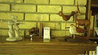 Full view of all decorative items on wooden shelf against brick wall including Inukshuk statue, elephant bookends, wooden birds and wooden antelope beside books