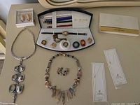 Overall layout showing silver-tone pendant necklace, stone chip necklace with matching earrings, clip-on earrings, two gold chains, Birks watch set, and Sheaffer pen box.