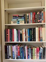 Three shelves of books with various hardcover, trade edition, and paperback novels, mostly orderly and stacked vertically with some horizontal stacking on top of others