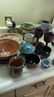 Overview of most pottery items arranged on a countertop including salad strainer, goblets, bowls, and small cups