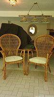 Pair of natural rattan chairs with curved backs and removable white seat cushions, placed indoors on tiled floor.