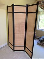Front view of the three-panel room divider set up showing the natural bamboo strips within a black wood frame.