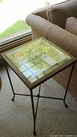 Side view of metal frame side table with beveled glass top placed next to a couch near window showing legs and frame detail.