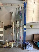 Four pairs of skis standing vertically, including two white Karhu pairs, one blue Rossignol downhill pair, and one white Salomon pair with poles, plus ski boots at base
