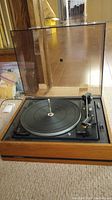 Turntable with wooden base, black platter, and lifted transparent dust cover showing the overall turntable unit.