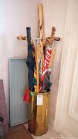 Photo showing hexagonal metal umbrella stand filled with several wooden walking sticks, canes and umbrellas, with two gray plastic boot trays leaning beside the stand.