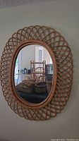 Full view of the oval wicker wall mirror hanging on a wall reflecting a room interior.