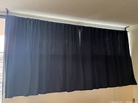 Black curtain panels hung on the longest rod, showing full and short lengths with some light exposure through fabric.
