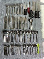 Assortment of mismatched metal forks, knives, spoons, and table cutting knives arranged on a white surface.