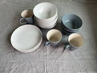 Photo showing the complete dishware set with gray mugs, white side plates, and two sizes of bowls in white and gray on a fabric surface.