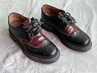 Front three-quarter view of both shoes showing black and burgundy wingtip leather uppers and round laces