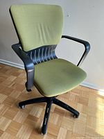 Green fabric office chair with black plastic frame and wheels, showing slight stain on seat and overall in lightly used condition.