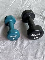 Photo of two hexagonal vinyl coated LifeGear dumbbells, one 5 lb in teal and one 10 lb in black, placed on a fabric surface.
