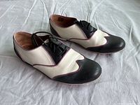 Right and left saddle shoes showing black and white leather with lilac piping, worn condition.