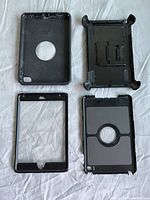 Top-down view of the four components of the OtterBox case for iPad Mini 4th Gen laid out on white fabric to show individual parts: back cover, inner plastic shell, front frame, and stand lid.