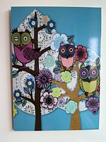 Photo of colorful owl print wall art with three stylized owls on trees with flowers, in blue background.