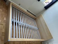 Queen size bed frame showing wooden slats base designed to support box spring and mattress with light wood veneer finish.