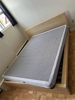 Photo of queen size box spring on a wooden bed frame showing the grey quilted fabric cover and condition of the box spring.