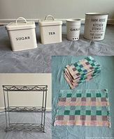 Four small canisters labeled Sugar, Tea, Garlic, and Kitchen Utensils, metal spice rack with two shelves, displayed on a surface.