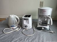 Photo shows set including white electric kettle, white two-slot toaster, and white drip coffee maker with glass carafe.