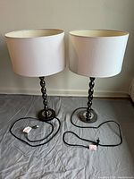 Pair of two table lamps standing side by side on a grey cloth background, showing full height with cords laid out in front.