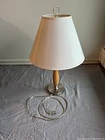 Full view of the table lamp showing metal base, wooden middle section, white fabric shade, and power cord.