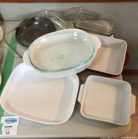 Top view of assorted Corningware white ceramic and clear glass baking dishes along with metal lids on a table.