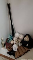 Photo of the baseball equipment lot against a white wall showing bat, gloves, various balls, a black cap and a small trophy