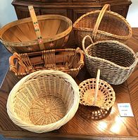 Photo showing six different baskets from a top view on a wooden table including a painted wooden basket and varied wicker baskets.