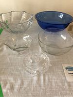 Five assorted decorative bowls including clear cut crystal, clear glass, and blue glass varieties are arranged on a table, showing size and shape variety.