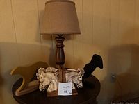Photo showing wooden table lamp with beige fabric shade alongside two carved wooden animal figurines: a black dog and dual white horse heads on a block.
