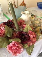 Artificial flowers and candle holder shown together with other decorative items on table.
