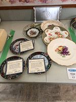 Overview of all decorative plates and the silver centennial tray, showing condition and arrangement on table.