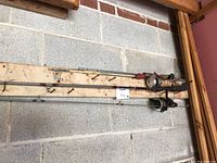 Two fishing rods with reels resting on wooden boards against a cinder block wall