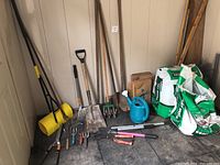Wide shot showing all garden tools including shovels, rakes, hand tools, watering can and peat moss bags