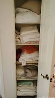 Closet shelves with multiple stacks of folded linens including white, beige, orange, purple, and green linens.