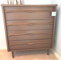 Front view of the mid-century modern style dresser showing four drawers with curved recessed handles and tapered legs.