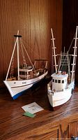 Two white wooden model ships on wooden surface, showing rigging and detailed parts