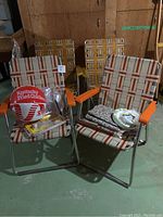 Four vintage folding outdoor garden chairs shown together. Two chairs have orange and beige stripes with orange plastic armrests; two chairs have yellow and beige stripes with yellow plastic armrests. Kentucky Fried Chicken bucket and disposable plates placed on chairs.